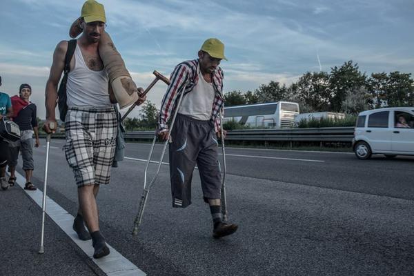 Two friends from Aleppo, Syria, walk 170km from Budapest to Austria to reach safety. One in socks and carrying his friends prosthetic leg. The other (who I understand lost his leg in the Syrian war) on crutches. (Photo: @DanielEtterFoto) 